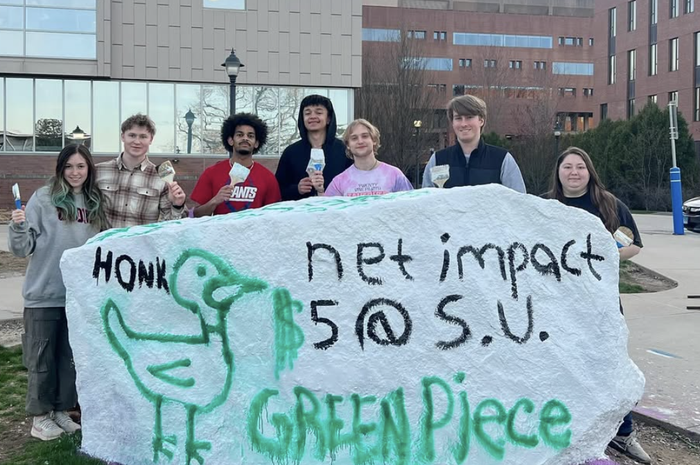 UConn Net Impact students posing behind a painted campus rock promoting sustainability and Green Piece initiatives